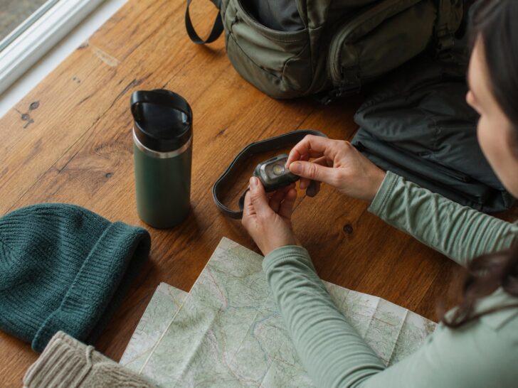 Hiker testing the controls on an unbranded headlamp beside a map and water bottle