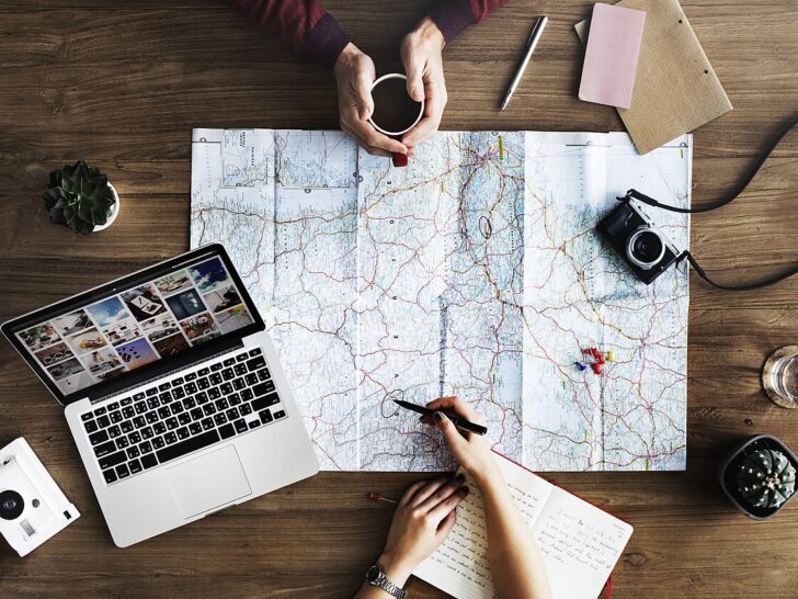 Two people planning a trip with a paper map, laptop, notebook, and coffee